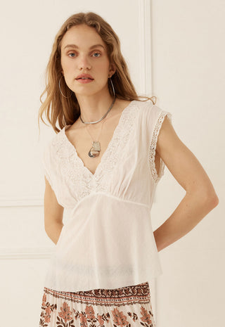 A woman wearing a white sleeveless lace-trimmed V-neck top with a gathered waist
